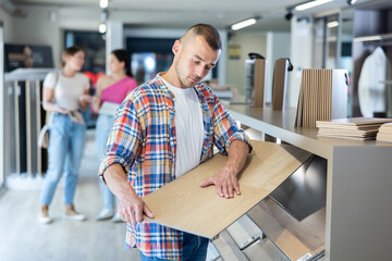 Young man buyer chooses sample of laminate flooring in hardware store