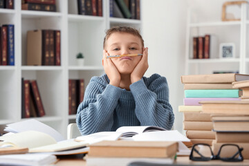 Tired teenage boy with pen and books at table in library