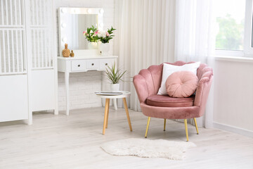 Interior of living room with pink armchair, chest of drawers, vase of flowers and coffee table