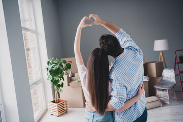 Rear portrait of two young people cuddle show heart symbol relocating moving box package new apartment indoors