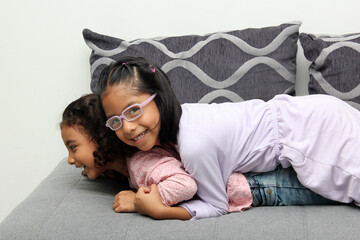 Two brunette Latina sisters of 4 and 5 years old play on an armchair and spend free time on a vacation weekend