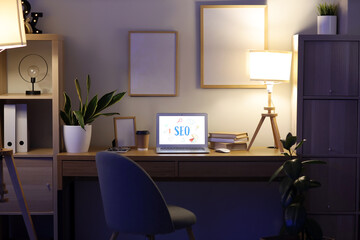 Laptop with abbreviation SEO on desk in dark office