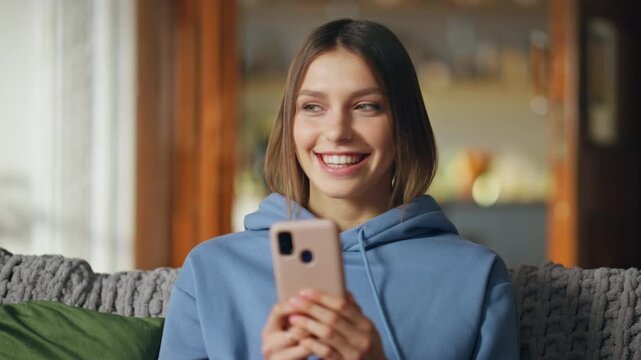 Happy girl typing cellphone sending message at home sofa closeup. Cheerful woman