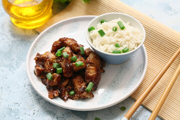 Tasty sweet and sour chicken with rice in plate, mat and chopsticks on blue grunge background, closeup