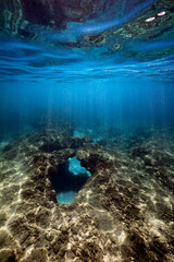 Obraz premium A underwater view of the clear blue waters and penetrating sun rays over a coral cavernous swim-through at Makaha, on the west coast of Oahu, Hawaii