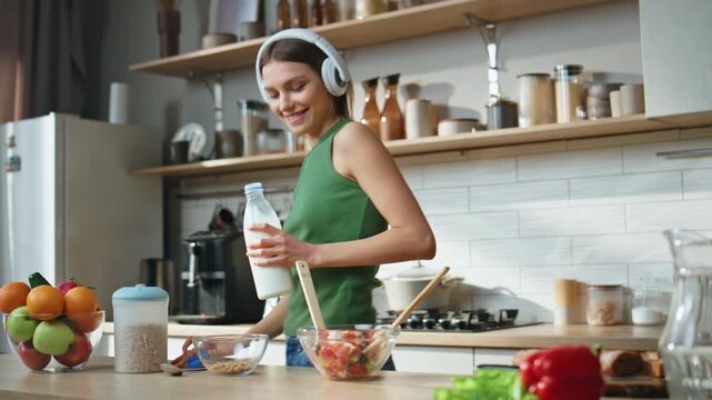 Cooking woman listen music in wireless headphones closeup. Girl pouring milk
