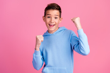 Photo portrait of cute teen boy raise fists winning dressed stylish blue clothes isolated on pink...