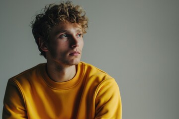 Fototapeta premium A young man looks off to the side, wearing a bright yellow sweatshirt