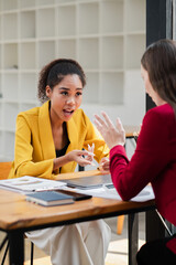 Two professional women engaged in a business meeting, discussing ideas and strategies in a modern office environment.