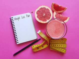 A glass of fresh grapefruit juice, notebook with weight loss plan, grapefruit slices and measuring...