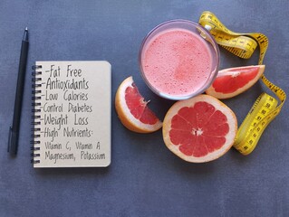 A glass of fresh grapefruit juice, notebook with health benefits of grapefruit, grapefruit slices...