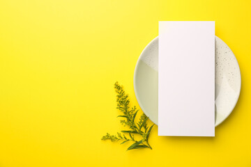 Empty menu, plate and floral decor on yellow background, top view. Mockup for design