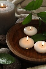 Burning candles and green leaves in water on table, closeup