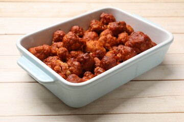 Baked cauliflower buffalo wings in baking dish on wooden table, closeup