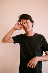 A Southeast Asian man rubbing his eyes due to itchiness, capturing a moment of irritation or...