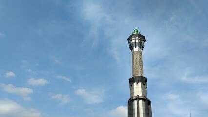 A low-angle view of mosque tower against a blue sky with wispy clouds.