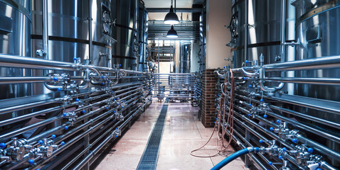 Sleek modern brewery interior with rows of shiny stainless steel tanks connected by intricate piping systems, emphasizing efficient craft beer production.