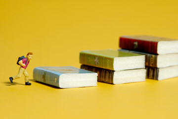 Miniature tiny people toy photography. A boy with school backpack standing above book stair....