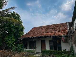 A weathered Indonesian house with a red tiled roof, surrounded by tropical greenery. The house shows signs of age and neglect, providing a glimpse into traditional rural living. abandoned house