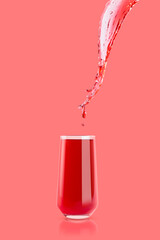 Red cherry juice. Stream of drink flow in drinking glass with bright splashes, drops flying, swirl on pink background. Vitamin cocktail with splashing for advertising, design, flyer, poster, card.