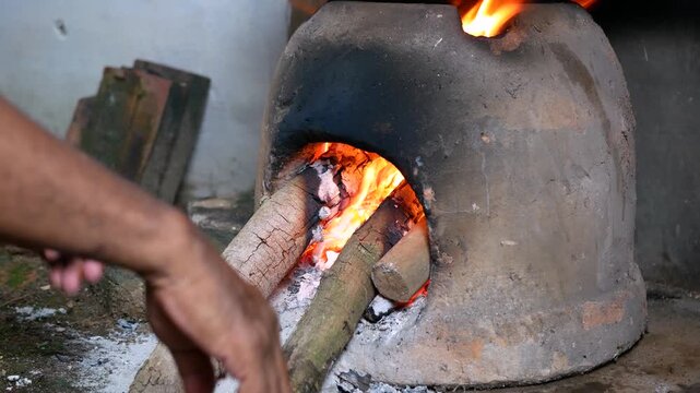 Close-up view of man arranging firewood in Earthenware furnace or tungku gerabah for cooking in traditional kitchen