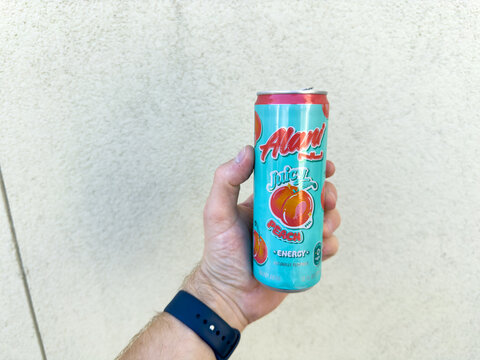 Alani Nu Peach Energy Drink Can Held Against Wall

