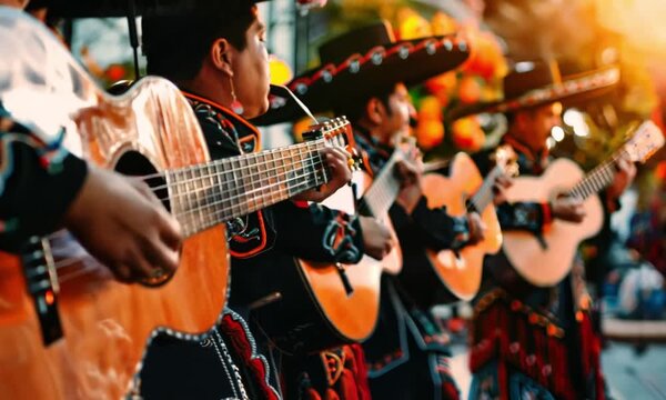 Musicians dressed in traditional mariachi outfits playing guitars at an outdoor event with warm lighting