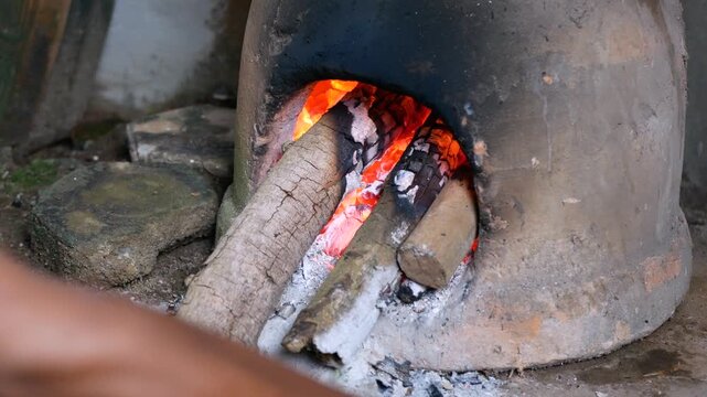 Close-up view of hand arranging firewood in Earthenware furnace or tungku gerabah for cooking in traditional kitchen