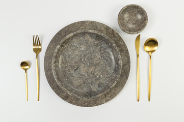 Top view of brown marble tray and plate, gold cutlery on white background. Food presentation, stone tray. Table setting, copy space, flat lay.