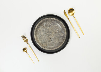 Top view of brown marble plate, black plate, gold cutlery on white background. Food presentation, stone tray. Table setting, copy space, flat lay.