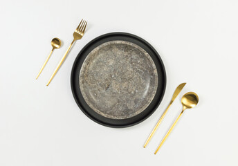 Top view of brown marble plate, black plate, gold cutlery on white background. Food presentation, stone tray. Table setting, copy space, flat lay.
