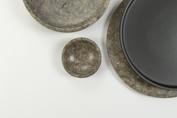 Top view of brown marble tray, black plate and bowl on white background. Food presentation, dishes, stone tray. Copy space, flat lay.