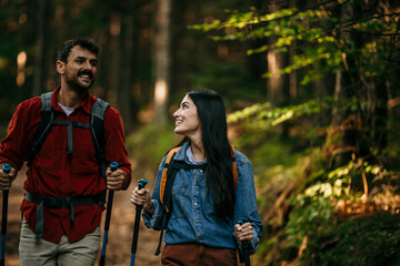 A multiethnic couple is in the forest hiking in the mountains choosing the best route to reach the summit