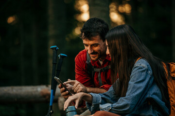 Happy couple of hikers using cell phone while relaxing in the forest