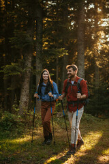 Fototapeta premium Young fit and healthy man and woman walking with sticks and backpack during hike in the woods