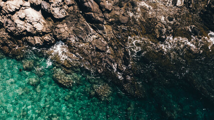 Aerial view of rocky coastline with turquoise water in Maui, Hawaii. The waves crash against the rocks, creating a beautiful contrast between the clear ocean and rugged shore.