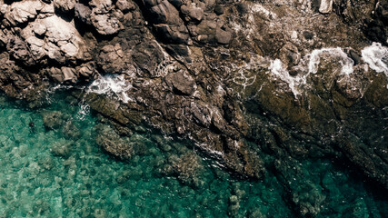 Aerial view of rocky coastline with turquoise water in Maui, Hawaii. The waves crash against the rocks, creating a beautiful contrast between the clear ocean and rugged shore.