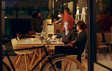 Night, computer and employee with mentor at desk for collaboration, feedback or project review. Advice, help and business women in discussion for learning, planning report or support in office