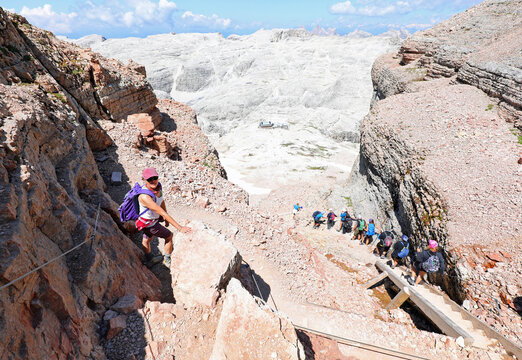 young girl with hat on her head with Frontino in backpack while descending a very steep path between a gully in the high mountains
