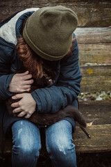 Teenager in old clothes sadly keeps and hugs black cat on his lap