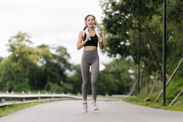 Happy fit Asian woman wearing headphones listening to music, wearing sports clothes, jogging in the city at sunrise. Beautiful young Asian woman in sports bra running outdoors Exercise in the morning.