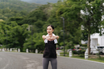 Young attractive Asian woman stretching her arms and legs before her morning exercise run at a running track of a local park