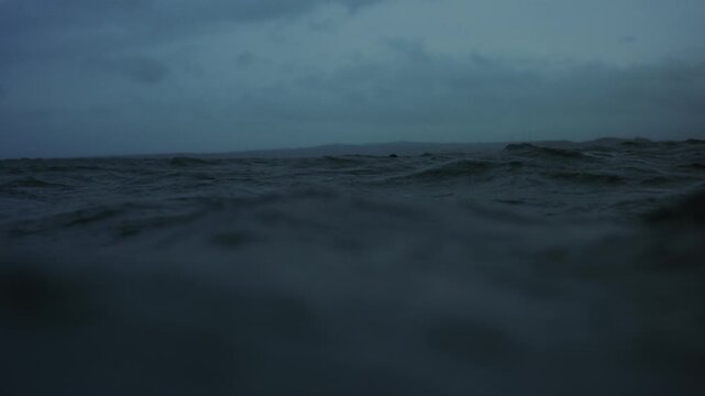 Head bobs in the distance behind ocean wave surface on stormy day in slow motion