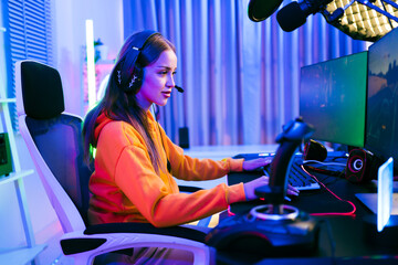 Young Caucasian woman professional gamer wearing yellow hoodie sits on a chair with a gaming table...