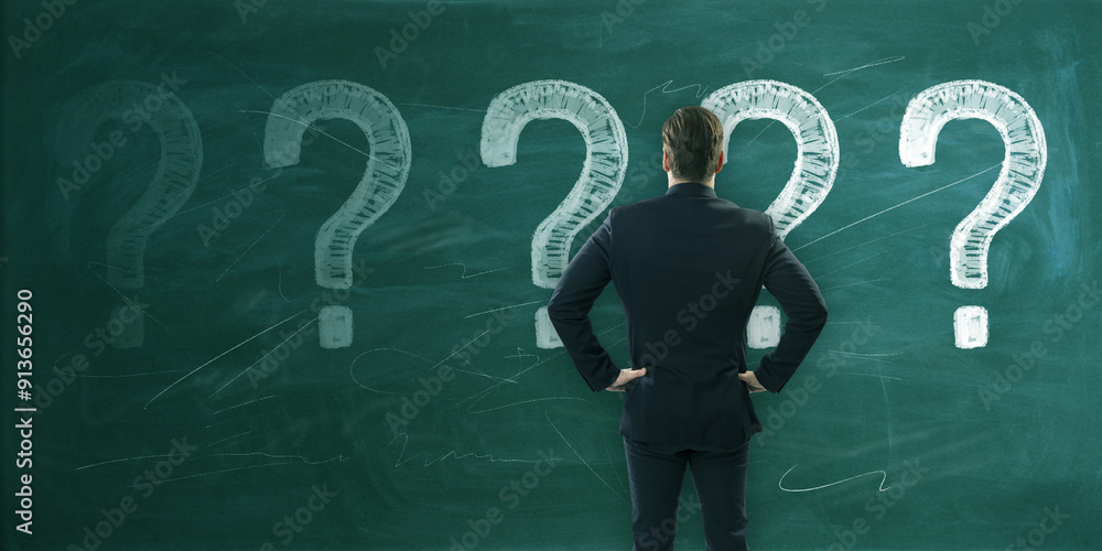 Poster back view of thoughtful young european man with chalk drawn question marks on blackboard background.