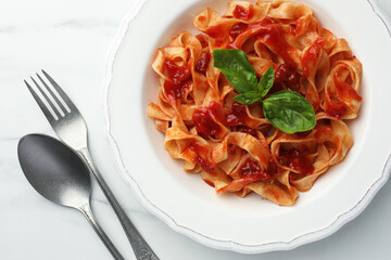 Delicious pasta with tomato sauce and basil served on white marble table, flat lay