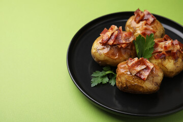 Fototapeta premium Delicious baked potatoes with bacon and parsley on green background, closeup. Space for text