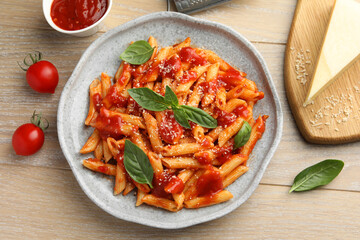 Delicious pasta with tomato sauce, basil and cheese on wooden table, flat lay