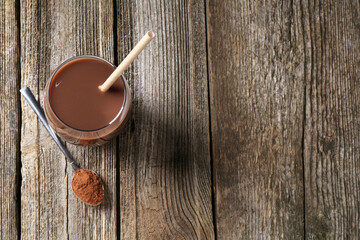 Delicious protein shake in glass and spoon with powder on wooden table, top view. Space for text