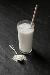 Delicious protein shake in glass and spoon with powder on black table